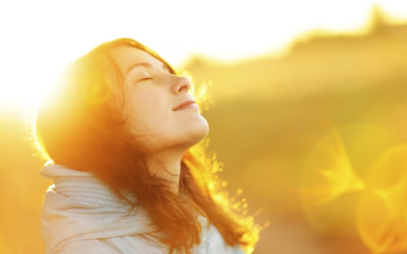 A photo of a woman in sunlight with her eyes closed and looking up