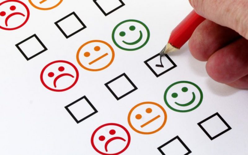 A photo of a person filling out a checkbox below an angry, neutral, and smiling emoji.